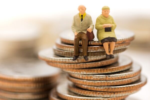 Figuras en miniatura de una pareja de ancianos sentados encima de una pila de monedas, que simbolizan el ahorro para la jubilación o la planificación de la pensión.