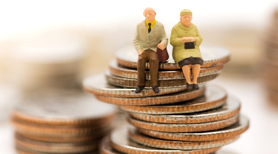 Figuras en miniatura de una pareja de ancianos sentados encima de una pila de monedas, que simbolizan el ahorro para la jubilación o la planificación de la pensión.